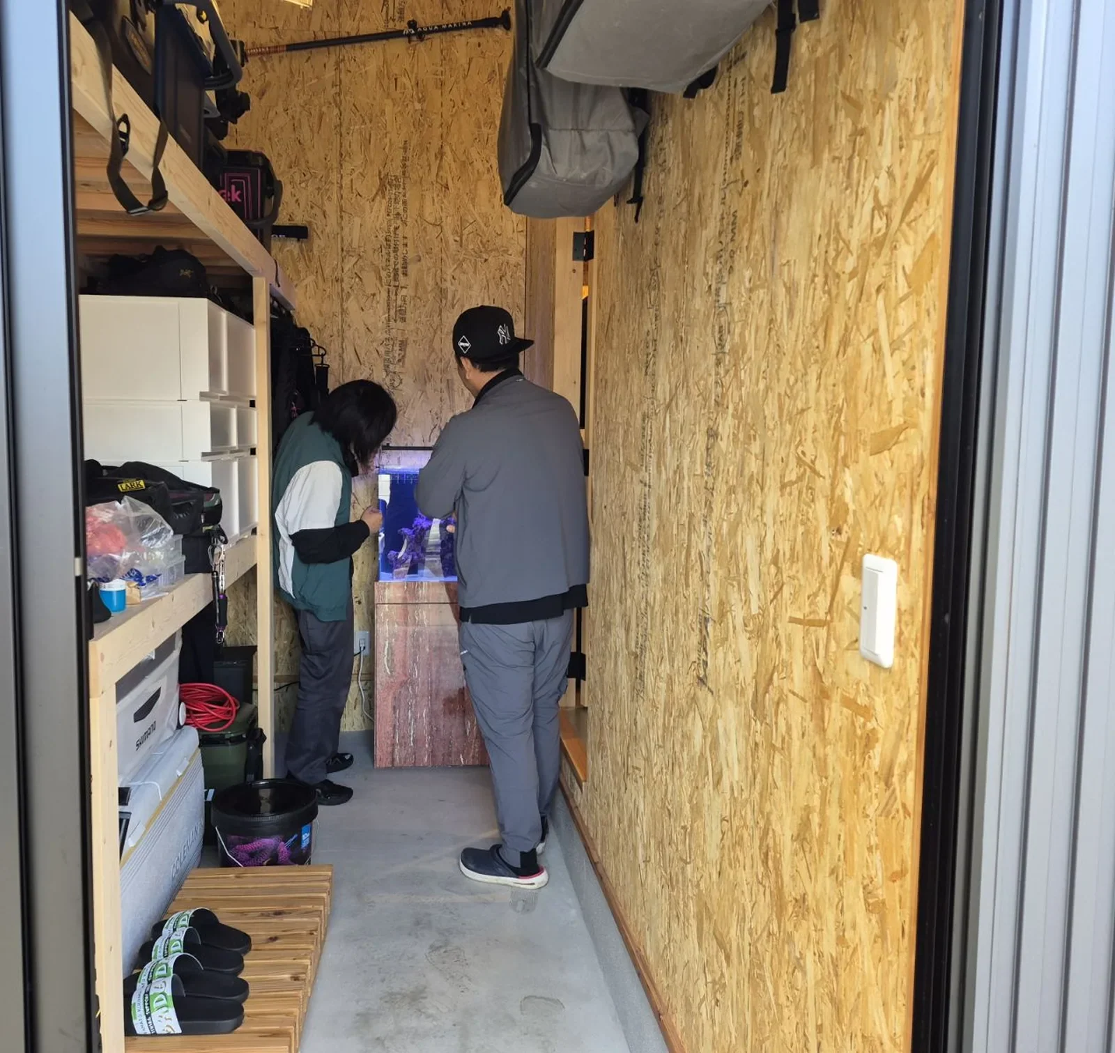 釣り道具が並ぶ趣味の小屋の奥に設置した水槽を確認するお客様とスタッフ